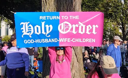 Participant in Oct. 12 rally holds a banner reading "Return to the Holy Order: God-Husband-Wife-Children"