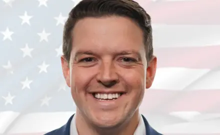 Portrait photo of Ryan Helfenbein, a smiling white man with faded US flag image in background