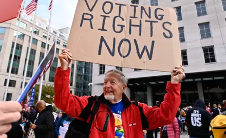 Older man holding a sign that says "voting rights now" 