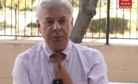 Lance Wallnau seated outdoors in shirt and tie, tree and fence visible behind him