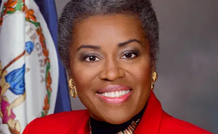 Close crop of official portrait of Virginia Lt. Gov. Winsome Earle-Sears, a black woman wearing a bright red suit jacket, with a Virginia flag visible over her right shoulder. 