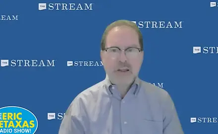 John Zmirak, a white man wearing a button-down shirt, is speaking in front of a background that repeats the logo for religious-right media outlet The Stream. The logo for The Eric Metaxas radio show appears in the lower left-hand corner of the screen. 