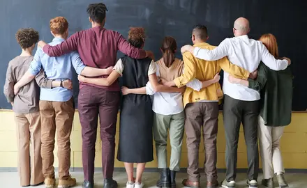 A group of people stand in front of a blackboard with their arms around each other