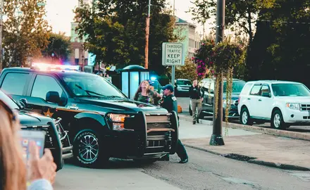 Two police arrest someone while a bystander films with a phone