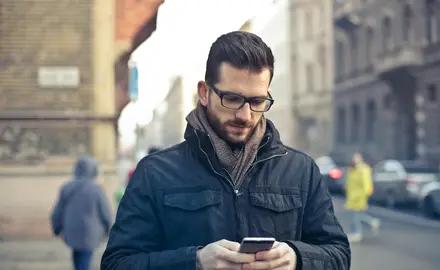 A white man stands on the street looking at his phone.