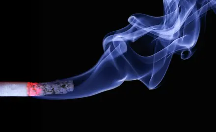 A cigarette releasing smoke in front of a black background