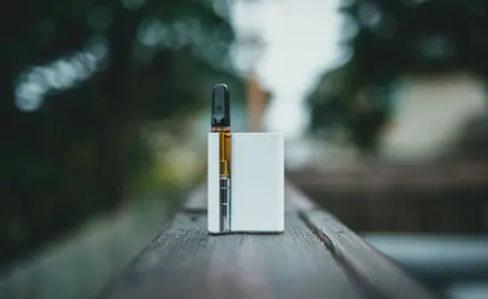 A photo of a white vape cartridge sitting on a fence