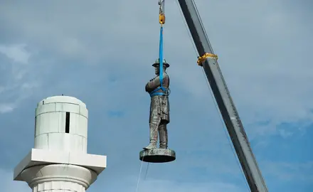 A state of Robert E. Lee is removed by a crane from its perch.