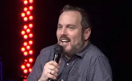Sean Bolz, a white man with reddish brown beard, dressed casually and holding a microphone