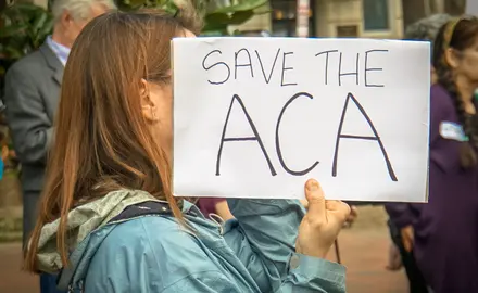A woman holds a sign that says "Save the ACA"