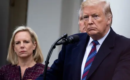 Donald Trump stands at a podium with Kirstjen Nielson