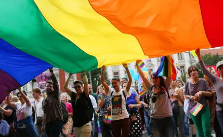 A group of people hold onto a massive rainbow flag