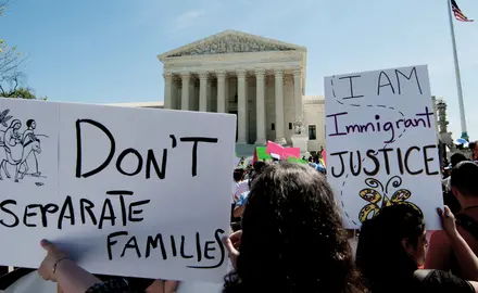 Rally-goers in front of the Supreme Court holding signs that say "Don't separate families" and "I am immigrant justice"