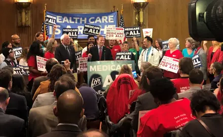 A group of people hold pro-Medicare signs in the senate.