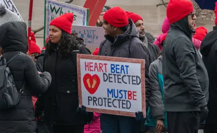 A group of anti-abortion protesters wearing red hats and holding signs that say "Heartbeat detected, must be protected"