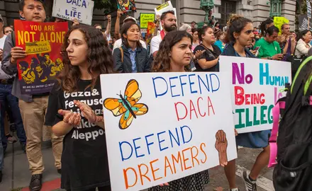 Activists hold signs saying "DACA = Life," "Defend DACA, Defend Dreamers," and "No Human Being Is Illegal" at a DACA rally.