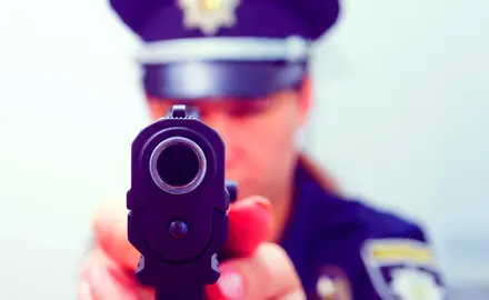 A police officer aims a gun directly at the camera