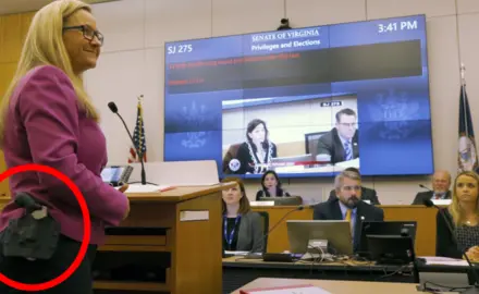 Amanda Chase stands at a podium and openly carries a firearm on her hip