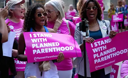 Protesters in Chicago hold pink signs that say "I stand with Planned Parenthood."