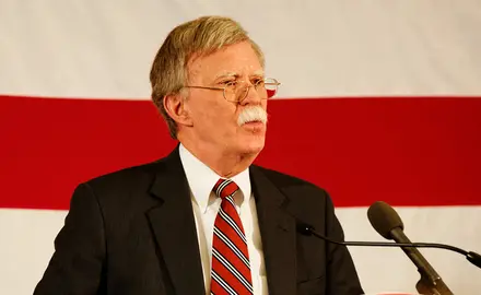 John Bolton stands at a podium in front of an American flag