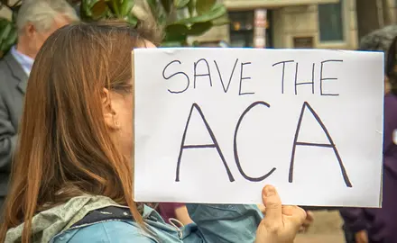 A woman holds a sign that says "Save the ACA"