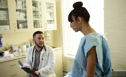 A transgender woman in a hospital gown speaking to her doctor, a