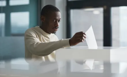 A black man deposits a ballot into a voting box.