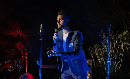 Rep. Maxwell Frost holds a microphone and speaks on a stage with musical equipment.