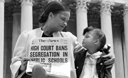 A woman and girl in front of the Supreme Court with a newspaper reading "High Court Bans Segregation in Public Schools"