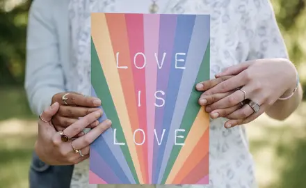 Two people holding a book with "Love is love" and a rainbow design on the cover.
