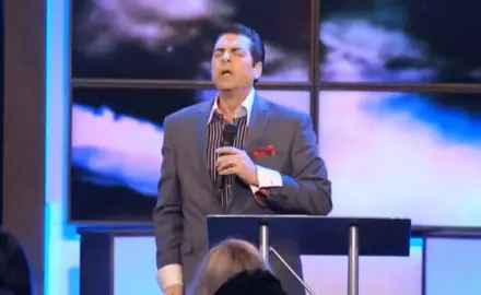 Hank Kunneman holding a microphone and standing at a podium.