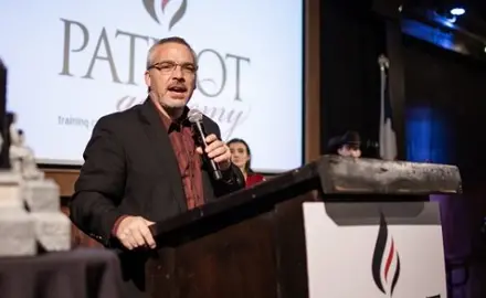 Rick Green standing at a podium and holding a microphone.