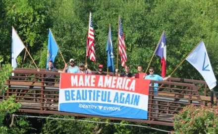 A group of white nationalists holding flags on a bridge.