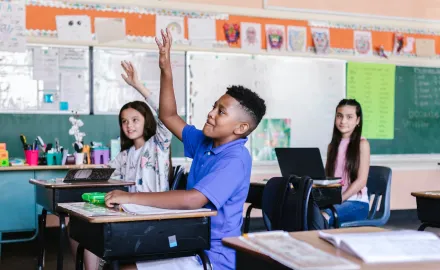 A Black child raising their hand in a classroom