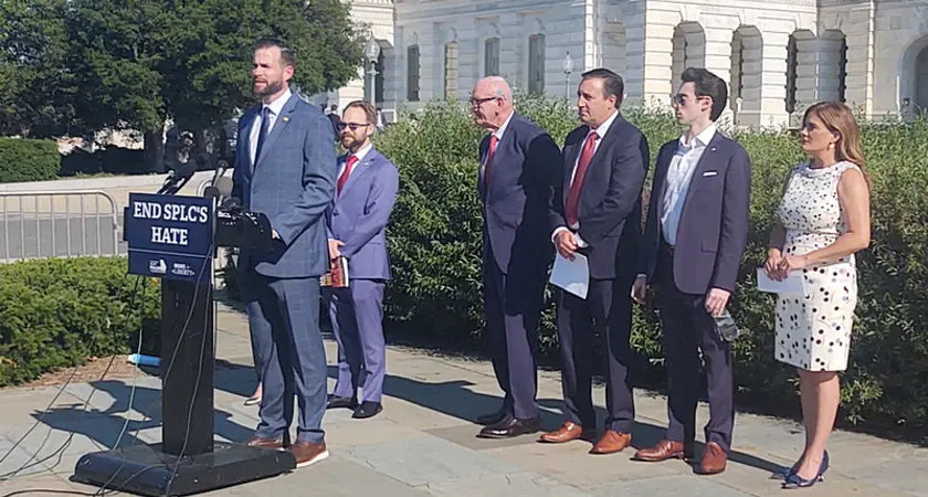 Photo shows Rep. Clay Fuller (R-GA) standing outside the US Capitol at a lectern with a sign that says "End SPLC Hate." Lined up behind him are five other people who spoke at the press conference, four men and one woman. 