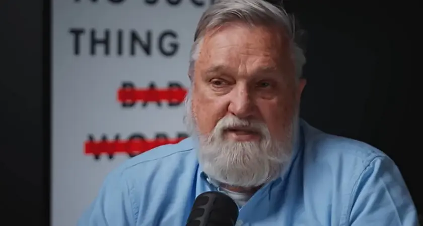 Doug Wilson, a middle-aged white man with gray hair and beard, is seated and speaking into a microphone. Partially visible behind him is an image of the cover of his book, "No Such Thing as Bad Words"