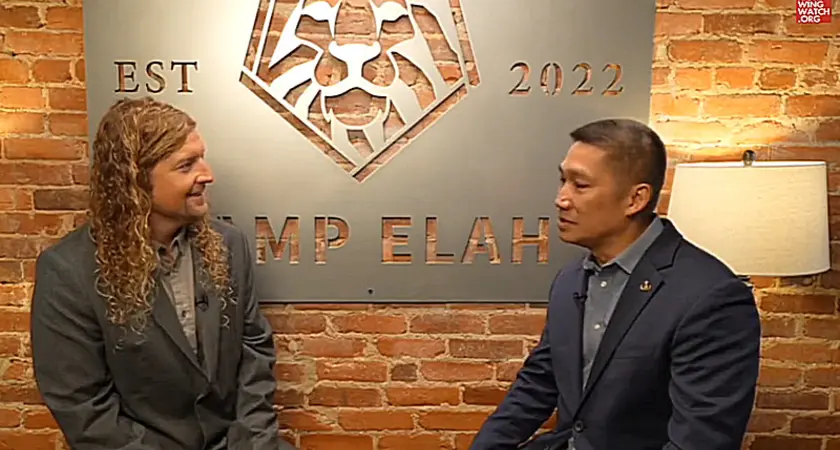 MAGA musician Sean Feucht and then-Senate candidate Hung Cao are seated in front of a brick wall on which is huge a large sign identifying their location as "Camp Elah," the Capitol Hill outpost for Feucht's political activities.