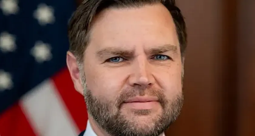 Close-up photo portrait of J.D. Vance with a blurry US flag visible behind him 