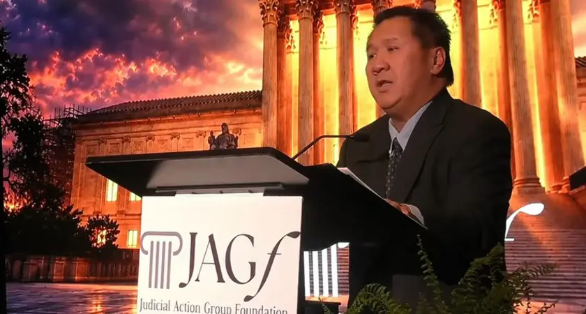 Judge James Ho stands behind lectern bearign logo of Judicial Action Network Foundation in front of backdrop image of U.S. Supreme Court lit dramatically at nightn