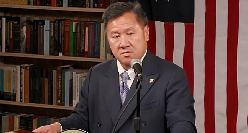 James Ho, in a suit and tie, speaks at a lectern with a U.S. flag visible behind him