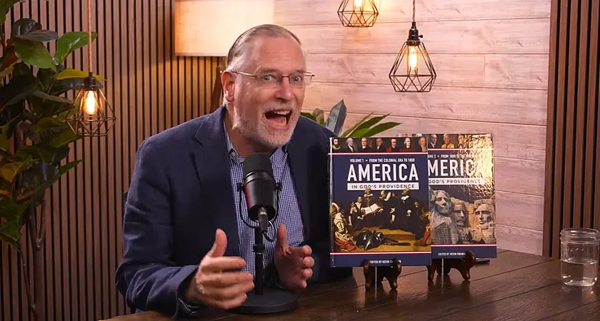 Kevin Swanson speaks animatedly into a microphone; two copies of his 1,000 page textbook on America's "Christian history" are propped up on the table next to him. 