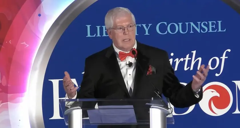 Mat Staver, a white man wearing a suit and red bowtie, gestures while speaking at lectern in front of logo for Liberty Counsel's 2025 gala and its theme "A New Birth of Freedom"
