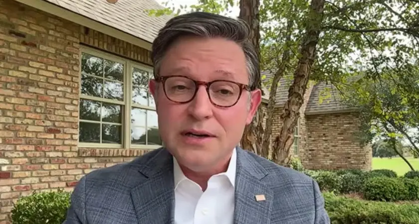 Mike Johnson, wearing suit jacket but no tie, is seated in his Louisiana back yard, with trees and his brick house visible behind him.