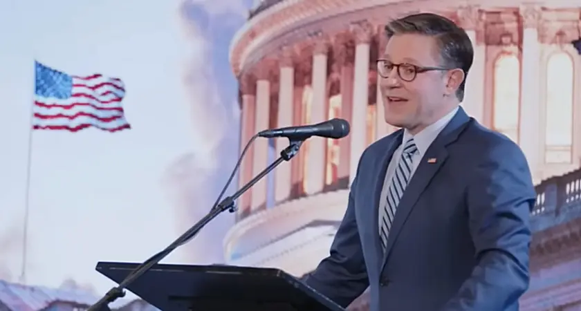 Image shows Mike Johnson standing and a lectern and speaking into a microphone in front of an illustrated image showing the Capitol dome and a U.S. flag fluttering in the breeze.