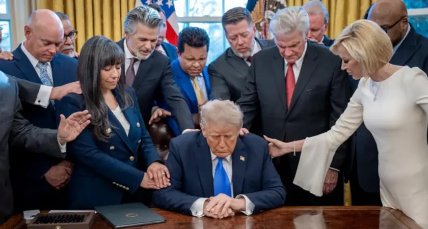 White House photo of Trump seated at his desk in the Oval Office surrounded by religious-right leaders; White House Faith Director Paula White, standing at right of image, lays her right hand on Trump's shoulder as she prays,