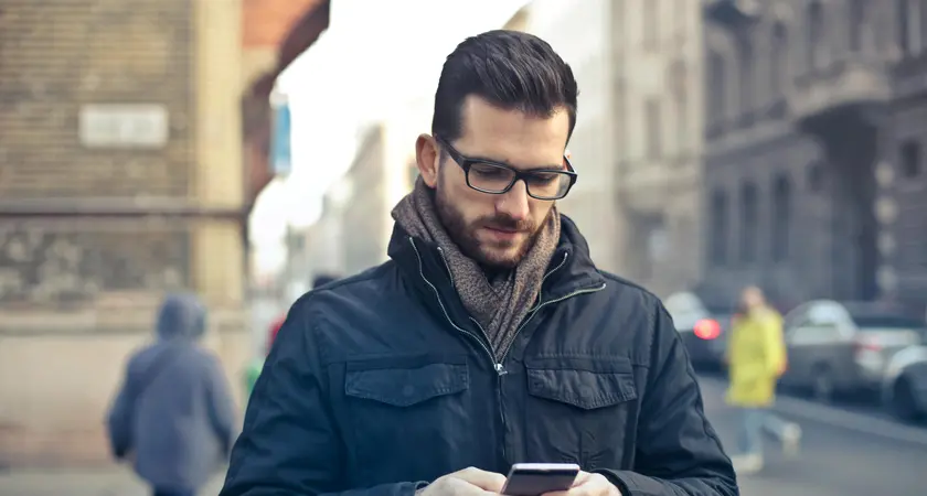 A white man stands on the street looking at his phone.