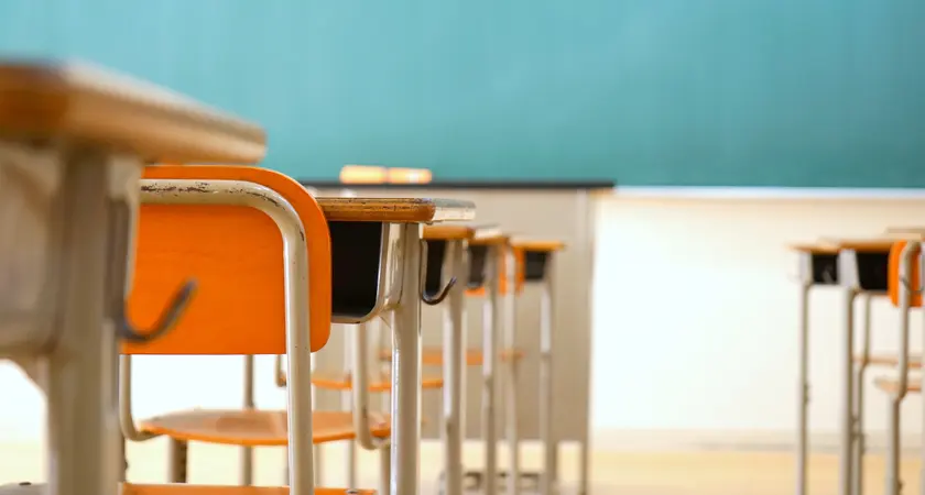 An empty classroom with desks and a chalkboard.