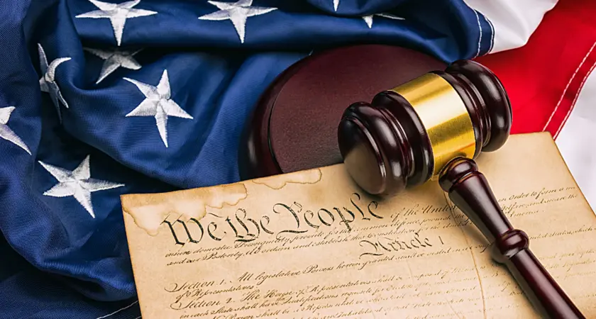 Picture of an American Flag and the U.S. Constitution with the phrase "We The People" clearly visible underneath a gavel.