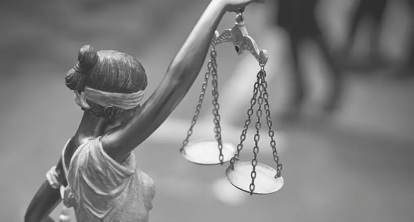 Black and white photograph of a statue of ablindfolded woman holding the scales of justice