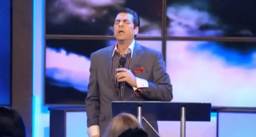 Hank Kunneman holding a microphone and standing at a podium.